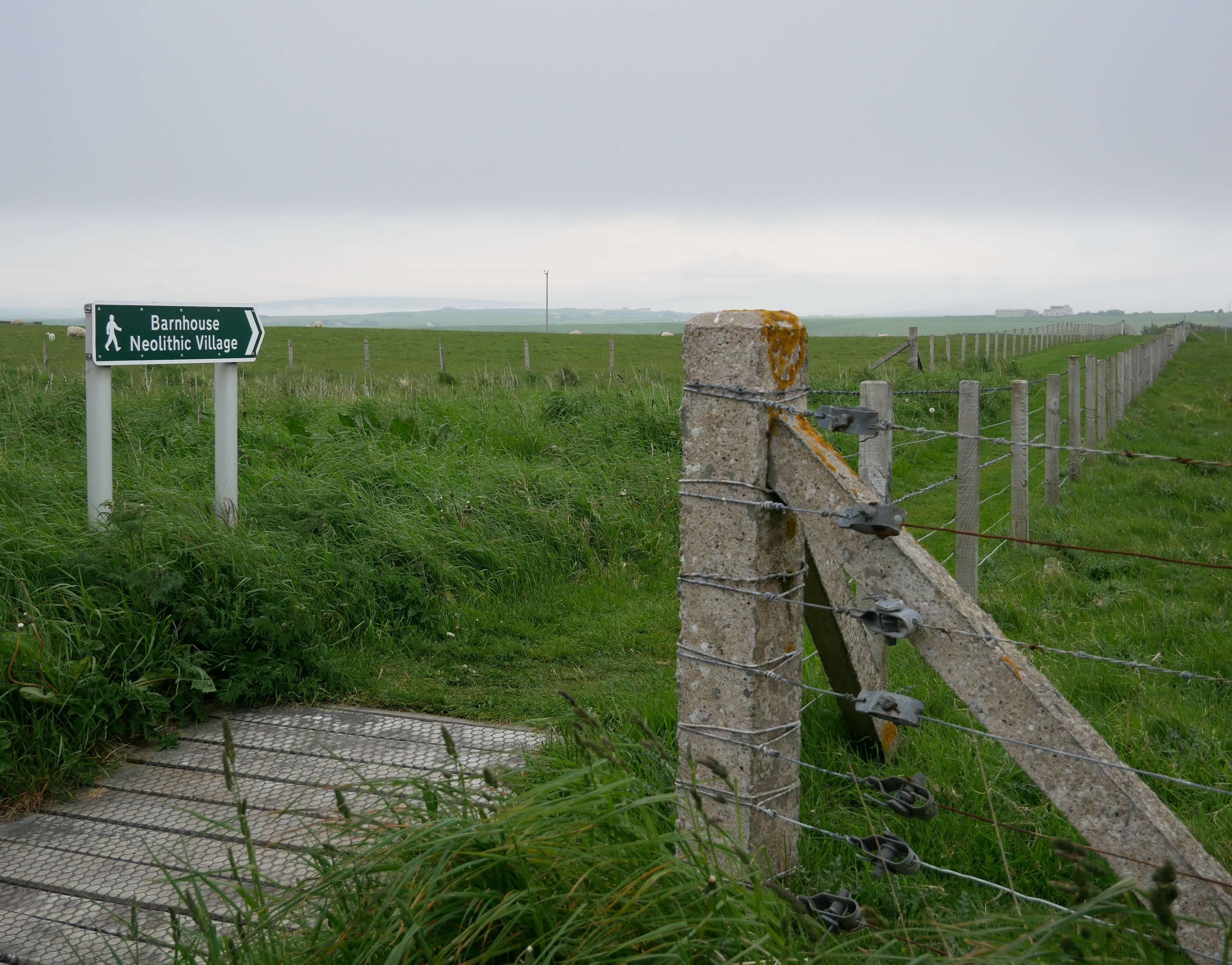 This way to Barnhouse Village - path is to the left of the stones Signpost for Barnhouse Village behind the standing stones at Stenness Loch, Orkney Islands, Scotland, UK. Orkneyology.com