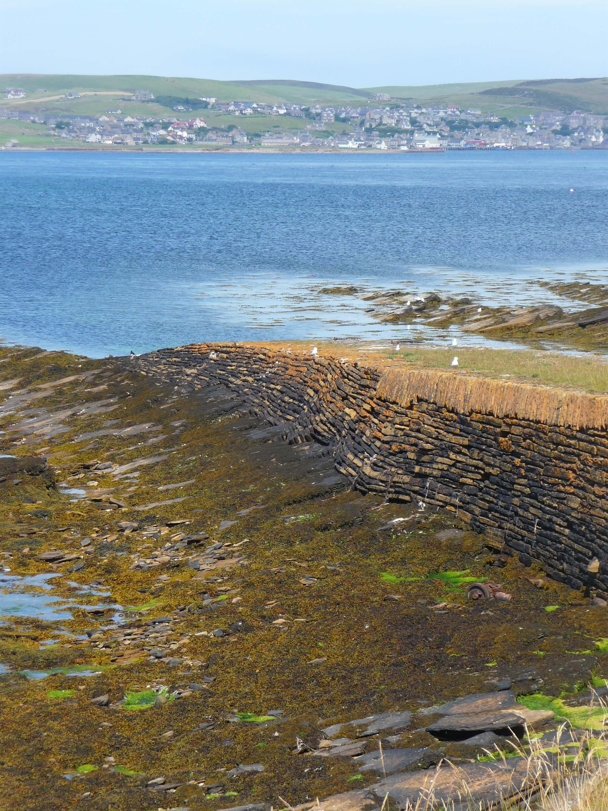 The old stone pier, with Stromness in the distance across the sound Old pier, Orkney island