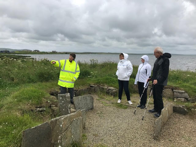 Orkney Islands tour guide Jo Jones guiding a group of Norwegians [photo by Erling Opdal 2019-07-06 at the Barnhouse Neolithic Settlement. Local Experts on Orkneyology.com